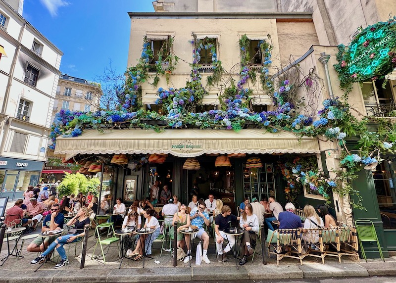 A sidewalk cafe covered in blue and purple flowers in Saint-Germain-du-Pres in Paris