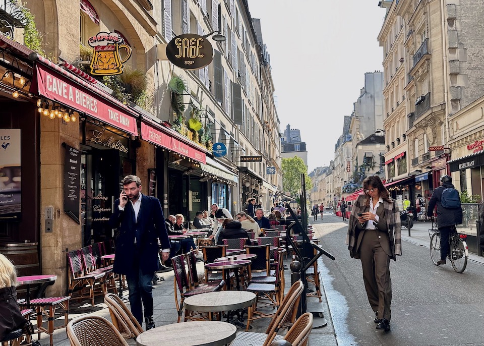 Chic Parisians passing through a sidewalk cafe on Rue De Buci in the Saint-Germain-des-Pres neighborhood of the 6th Arrondissement of Paris