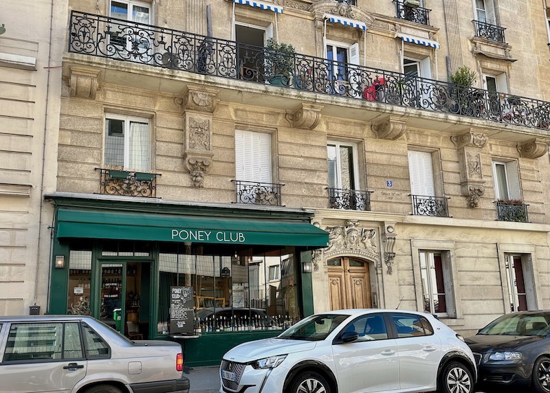 The green awning and exterior of the Poney Club wine bar on the ground floor of a Haussmann building in Montmartre, Paris