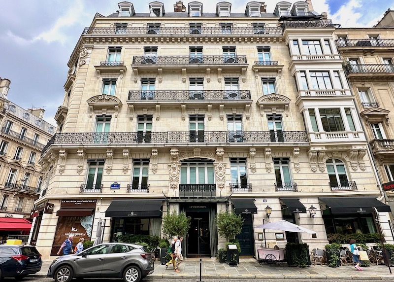 Haussmann-style facade with ornate iron balconies, dormer windows on top, and a glass canopy above the entrance at the Grand Powers hotel in the 8th Arrondissement of Paris