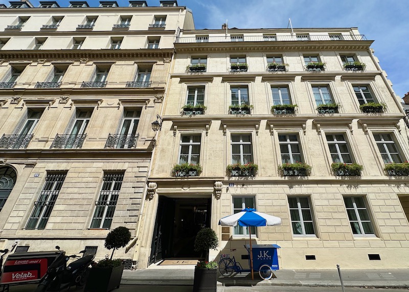 Street view of the understated entrance to JK Place with potted plants at each window and an ice cream cart in front in the 7th Arrondissement of Paris