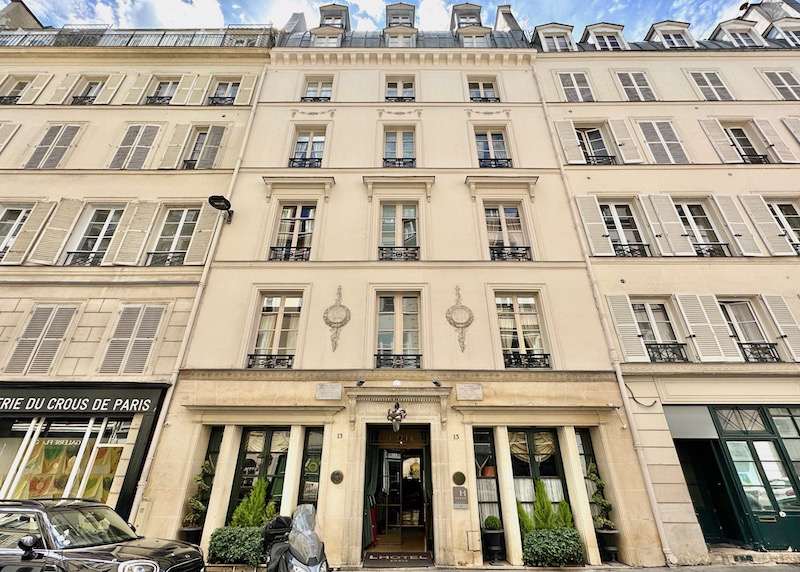 Grand Haussmann-style exterior of L'Hotel with a two tiers of dormer windows on top and iron railings below each window in the 6th Arrondissement of Paris