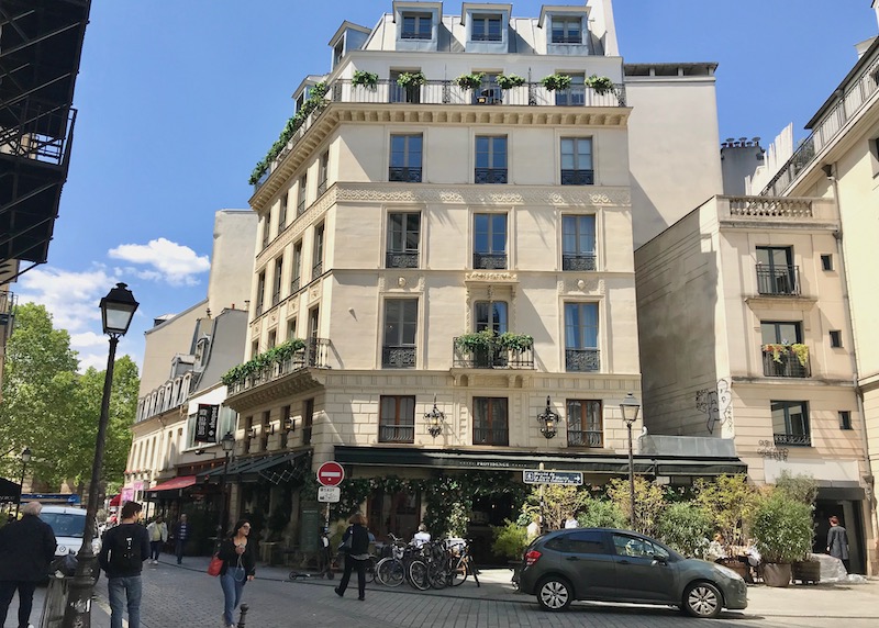Understated 19th-century facade with iron balconies draped with green plants and dormer windows on top in the 10th Arrondissement of Paris