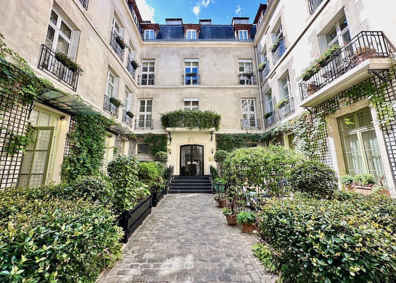 Leafy green courtyard entrance with a cobblestone walkway at Relais Christine hotel in the 6th Arrondissement of Paris