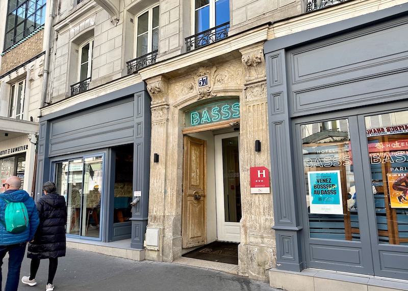 The stone entrance of the Hotel Basss flanked by grey facades in the 18th Arrondissement of Paris