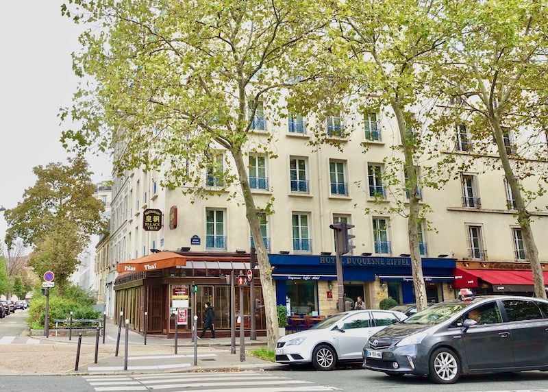 Exterior of the Hotel Duquesne Eiffel with restaurants on both sides and a tree-lined sidewalk in the 7th Arrondissement of Paris