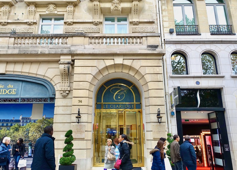 The Belle Epoque facade of Fraser Suites Le Claridge in Paris with a stone arched doorway, brass and glass entrance, and carved faces above the windows.