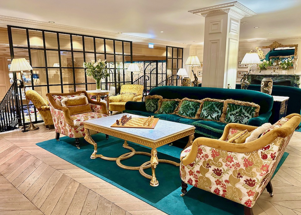 The salon of the Relais Christine hotel in Paris with plush, vintage-inspired furnishings in emerald green, gold, and scarlet