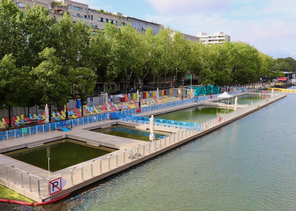 Four outdoor pools with rows of umbrellas and a line of green trees at Bassin de la Villette in Paris