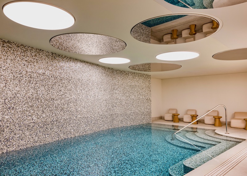 Tiled pool with steps leading into the water, a row of chairs, and round mirrors on the ceiling at Kimpton St. Honore in the 2nd Arrondissement of Paris