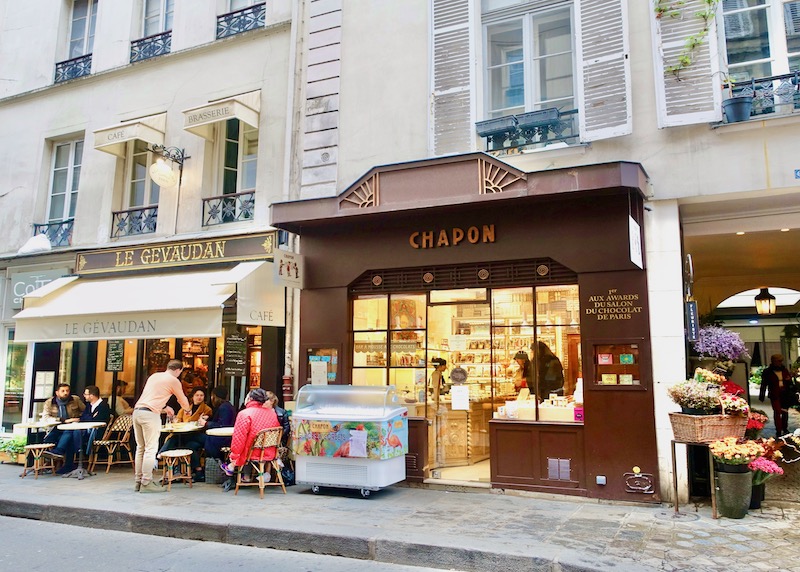 Brown exterior of Chapon chocolatier with warm gold light within the shop in Paris