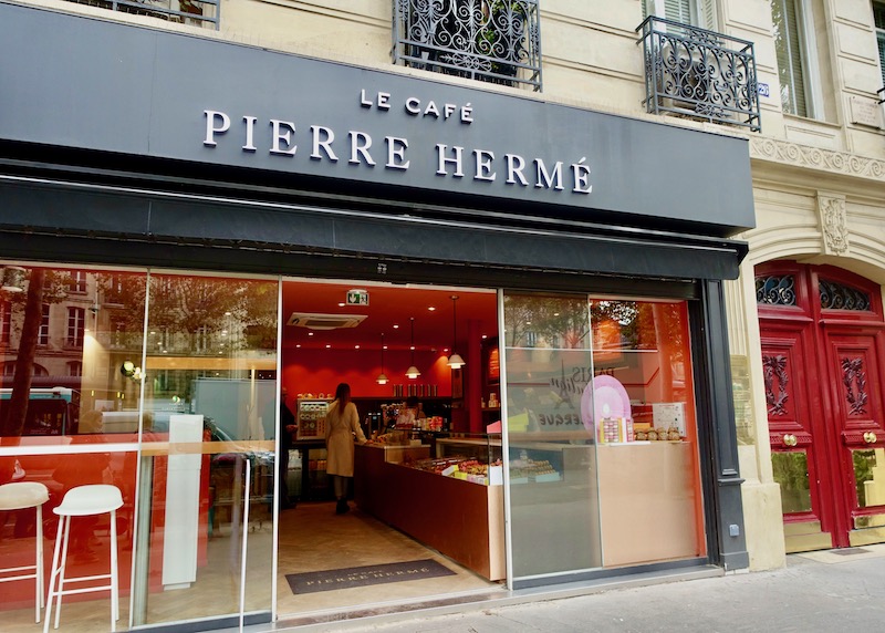Warm red interior shown beyond the glass doors of Pierre Hermé cafe and patisserie in Paris