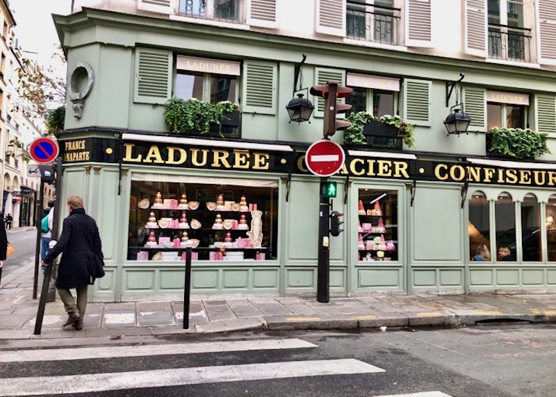 Green exterior of Ladurée patisserie with pink and gold treats displayed in the windows in Paris