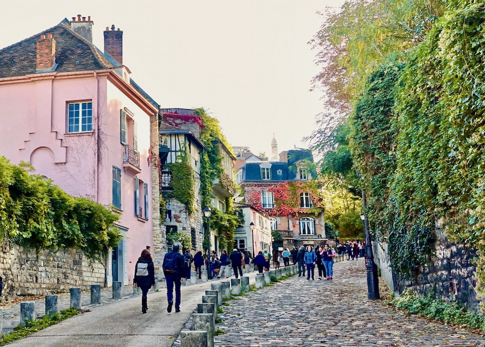 A curved cobblestone street leads uphill past traditional houses covered in ivy