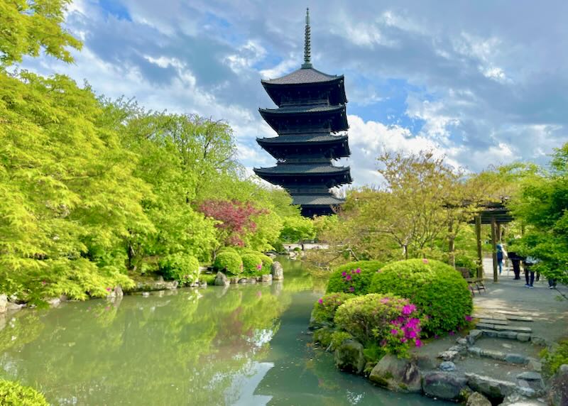 A dark multi-level canopy roofed temple rises to the sky over a lush green pond.