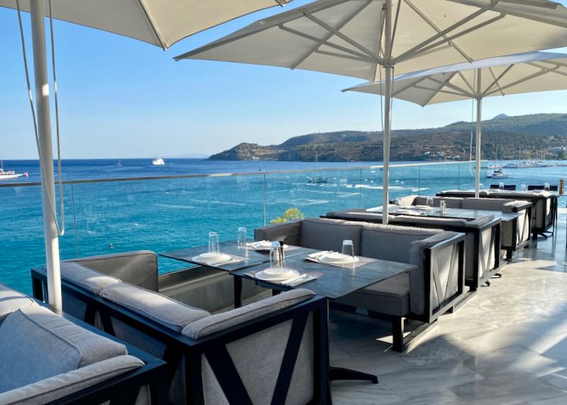 Elegant dining tables, shaded by sun umbrellas, overlooking the sea