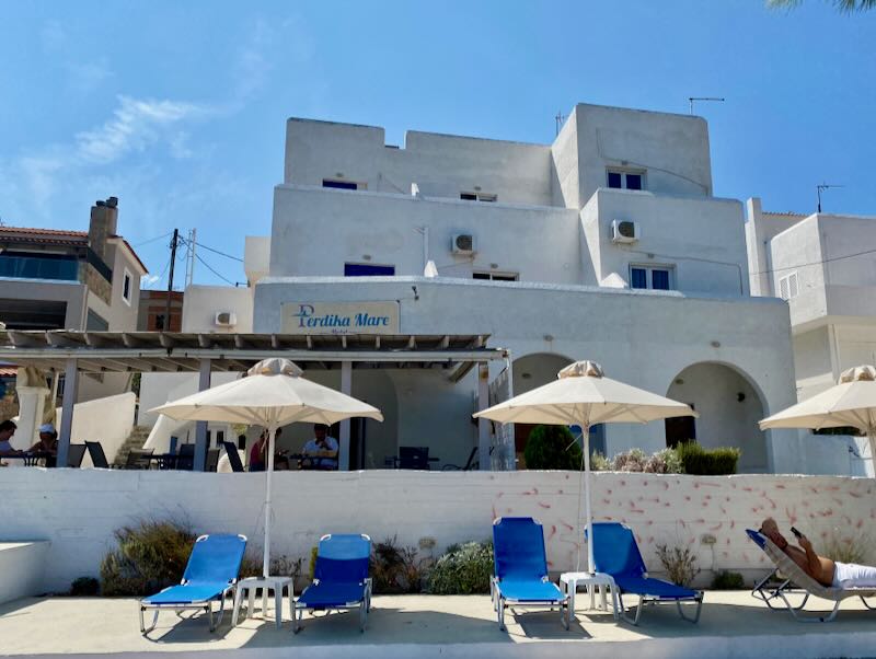 Sun loungers shaded by beach umbrellas sit in front of a boxy white hotel on a sunny day