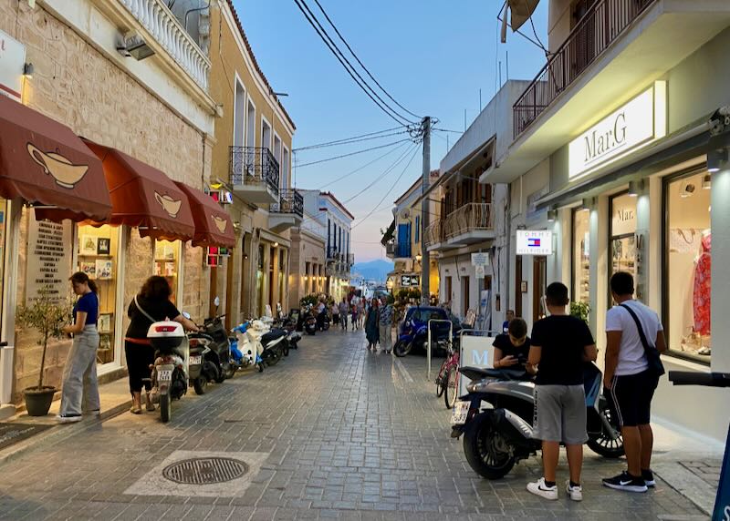 People congregate and shop in a narrow street leading to the sea at dusk