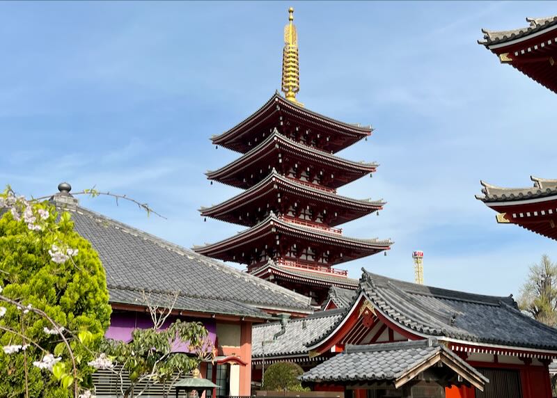 A red-tiered pagoda-like temple rises above lower shrines on a sunny day