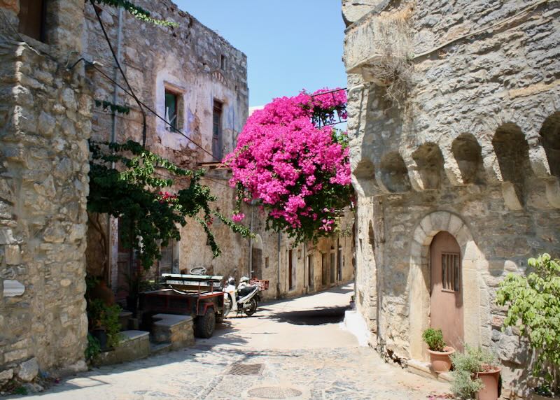 Small curved road lined with rustic stone buildings overhung with bouganvila