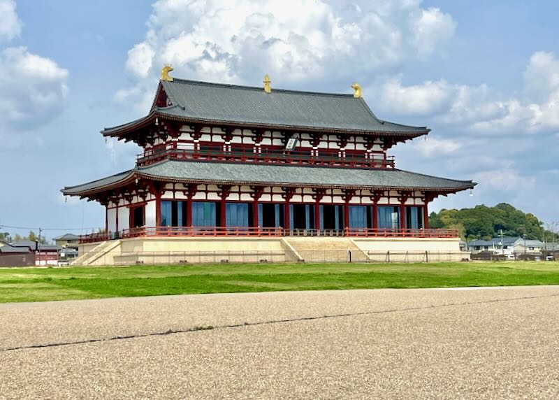 A large building with red wood pillars and two levels sits in a park.