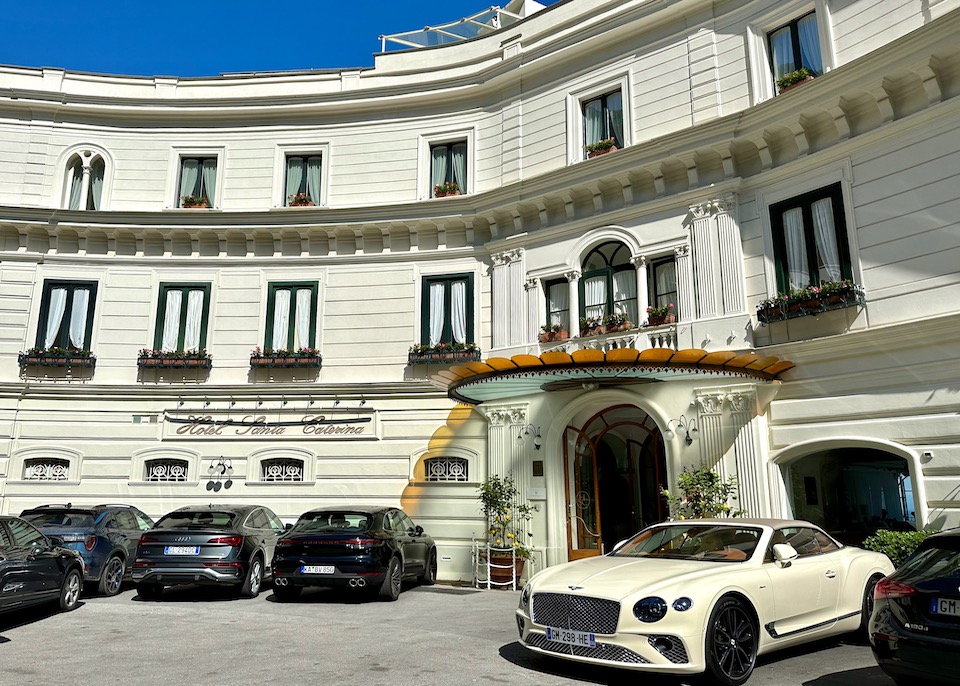 Exterior and main entrance of Hotel Santa Caterina in Amalfi with an Art Deco awning and luxury cars parked in front.
