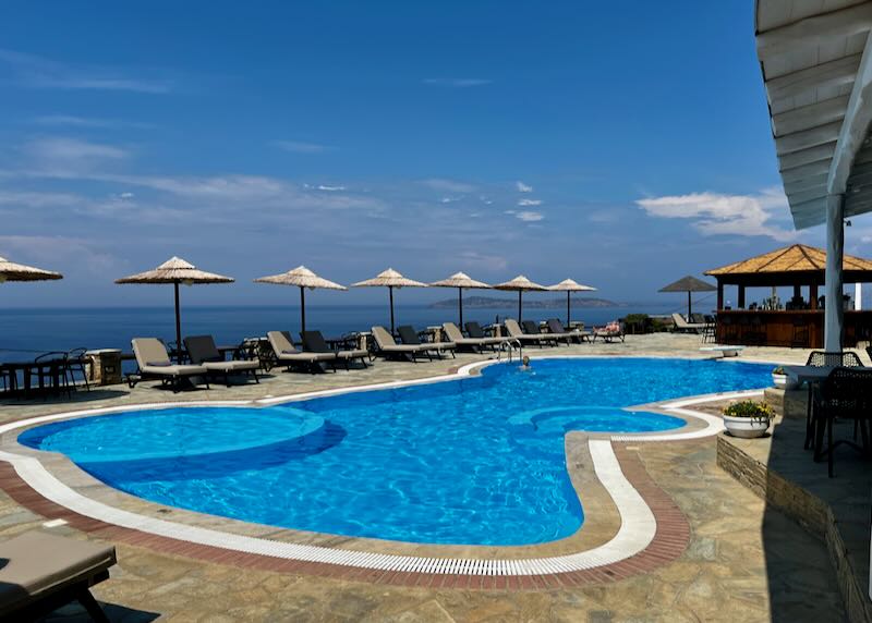 Blue swimming pool lined with sin beds overlooking the blue Aegean Sea