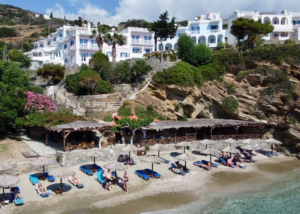 White hotel on a hillside above a sandy beach lined with thatched umbrellas