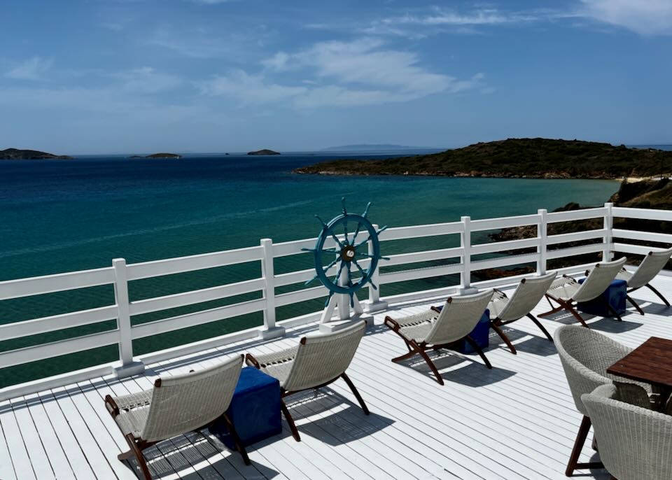 White wooden deck with tables and chairs above the blue sea
