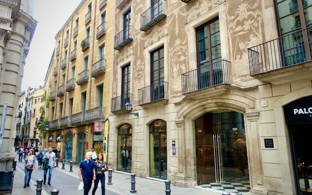 Exterior of an apartment building in Barcelona, with frecscoed walls and pedestrians walking by