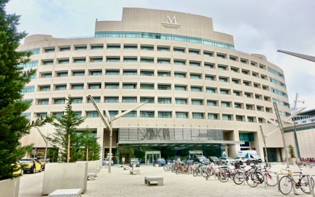 Large modern hotel with many cars and bikes parked in front