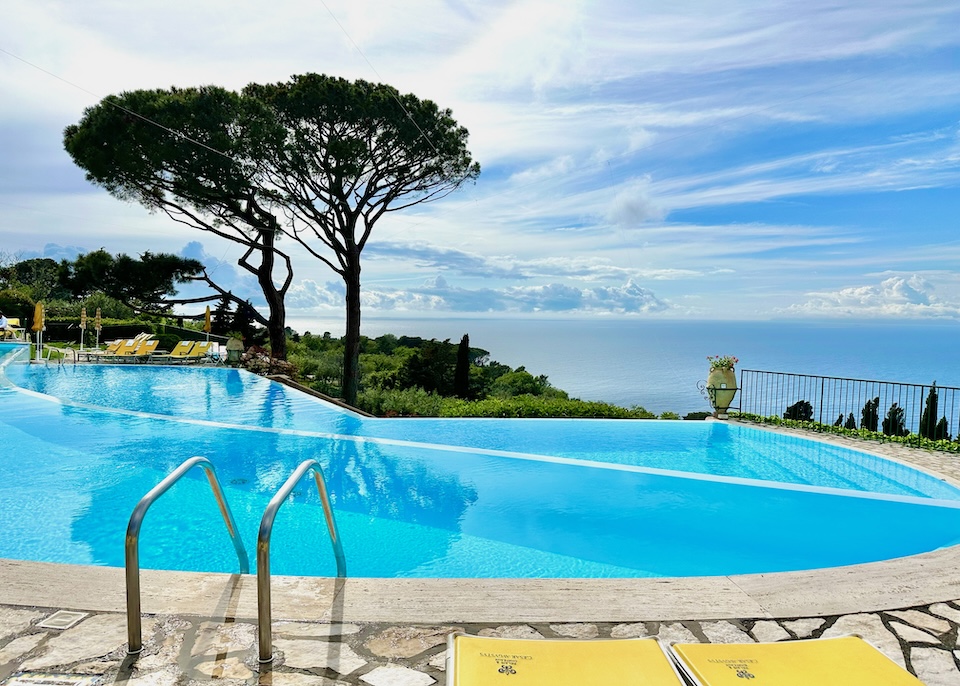 Split-level infinity pool facing the sea with yellow sunbeds and trees at Hotel Caesar Augustus in Anacapri, Capri