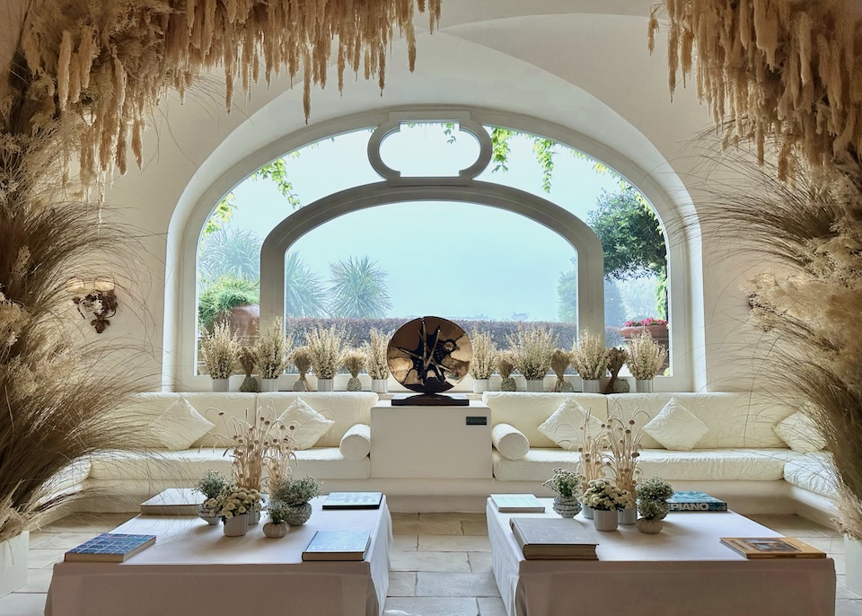 In the lobby with a built-in wraparound sofa, vaulted ceiling, and floral arrangement with dried grasses at Capri Palace Jumeirah in Anacapri, Capri