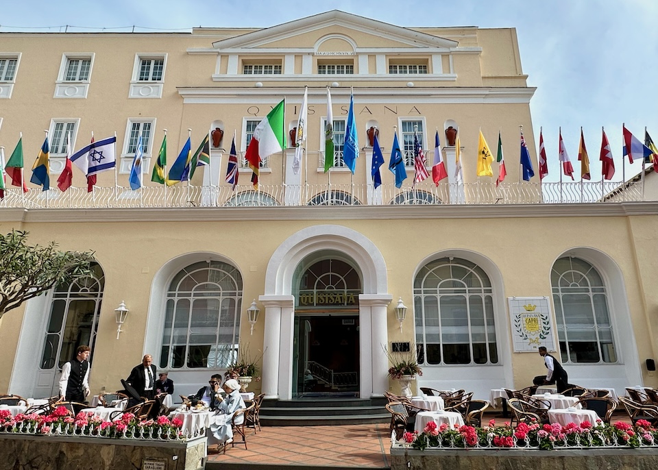 Exterior of Hotel Quisisana with arched door and windows, a dining terrace, and international flags in Capri Town