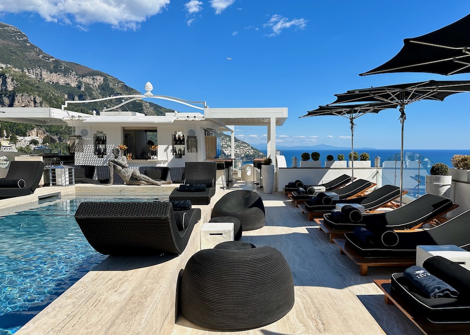 Rooftop pool lined with black sunbeds and umbrellas served by a bar and overlookiing the sea at Hotel Villa Franca in Positano on the Amalfi Coast
