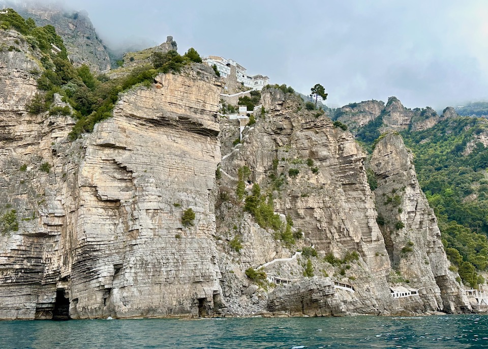 The white main building of Grand Hotel Tritone on tope of a sheer cliff with a zigzag staircase down to the beach club and sea in Praiano on the Amalfi Coast