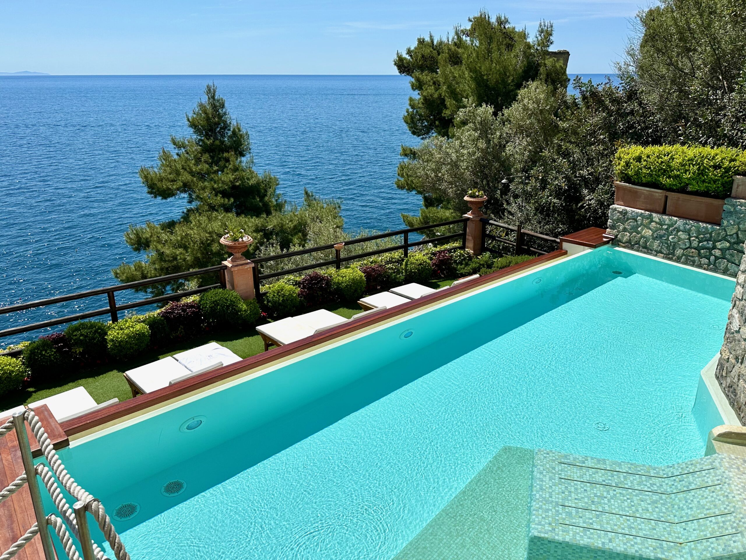 Infinity pool with a sunken lounge chair inside and a row of sunbeds facing the sea at Hotel Onda Verde and Villa Corallium in Praiano on the Amalfi Coast