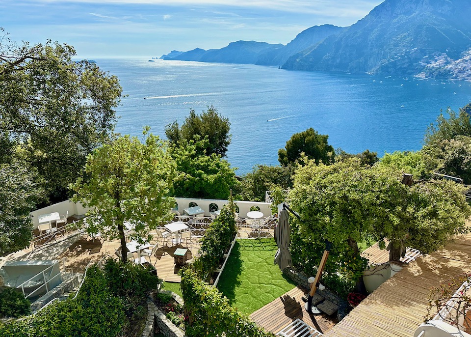 View over the trees and dining terrace toward the sea and mountainous coastline at Piccolo Sant'Andrea in Praiano on the Amalfi Coast