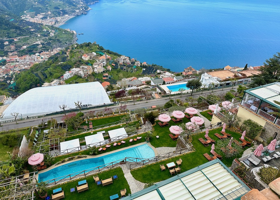 View from above Palazzo Avino in Ravello with a pool, grassy lawn, and pink umbrellas overlooking the Amalfi Coast.