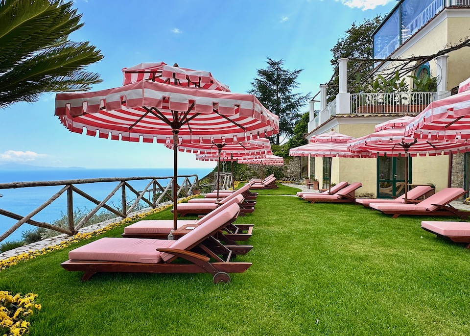Pink and white striped umbrellas and sunbeds on a lush lawn overlooking the sea at Palazzo Avino in Ravello on the Amalfi Coast
