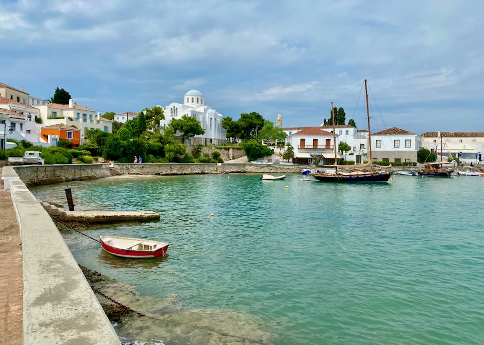 Blue-green bay with fishing boats and a white Greek church in the background