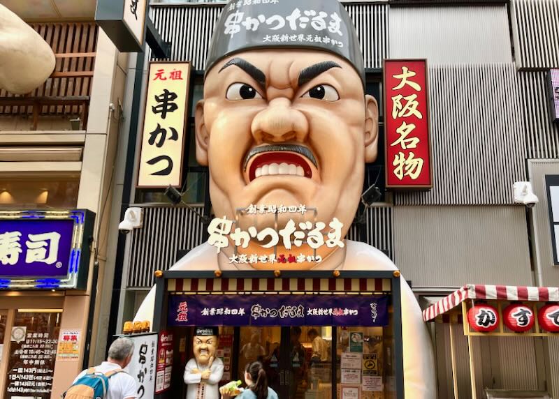 A large relief sculpture of an angry chefs face sits above the opening of a restaurant.