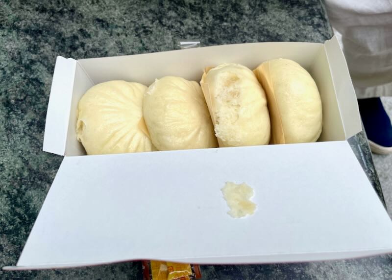 A box with four light yellow buns filled with pork.