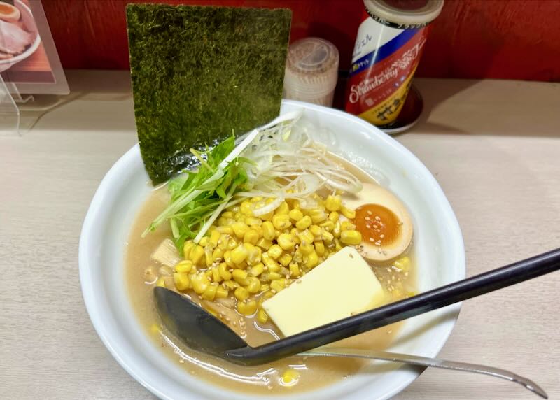 Corn, butter, a boiled egg, and green onion sit in a broth in a soup bowl garnished with seaweed.