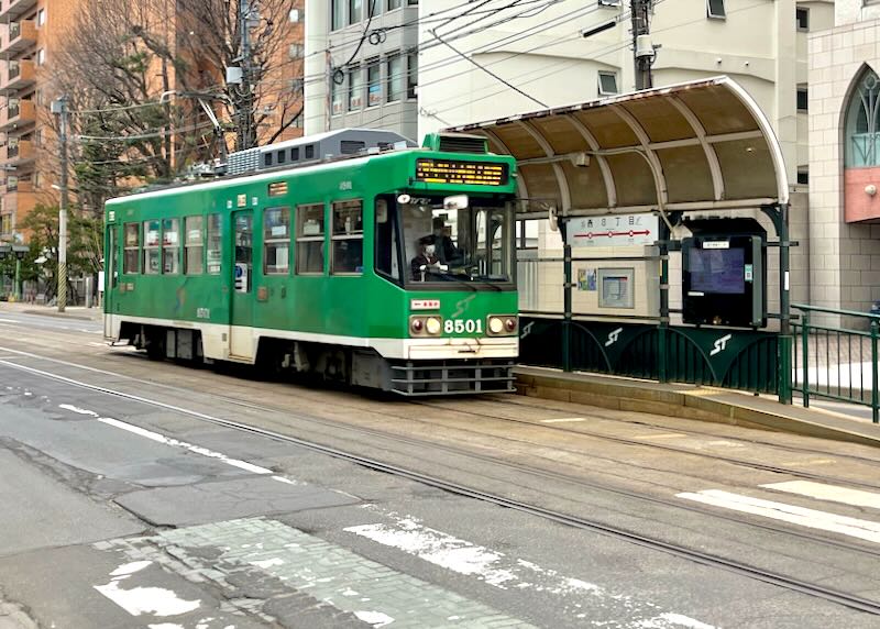 A green tram approaches a stop.