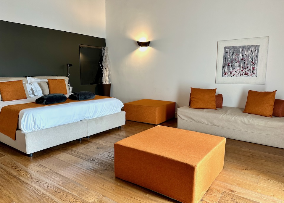 Inside a suite with a king bed, sofa and orange accents at Artemesia Domus hotel in Naples, Italy