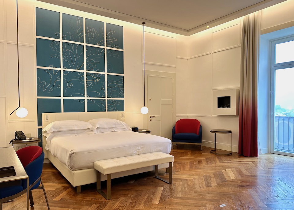 Inside a junior suite with a king-sized bed, coral wall art in turquoise and gold, and parquet floors at The Britannique in Naples, Italy