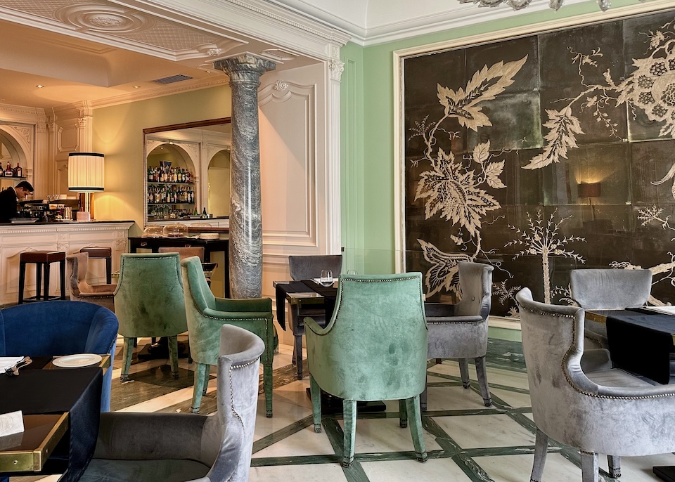 An opulent bar with velvet chairs, a marble column, and floral themed wall art at Santa Lucia Hotel in Naples, Italy