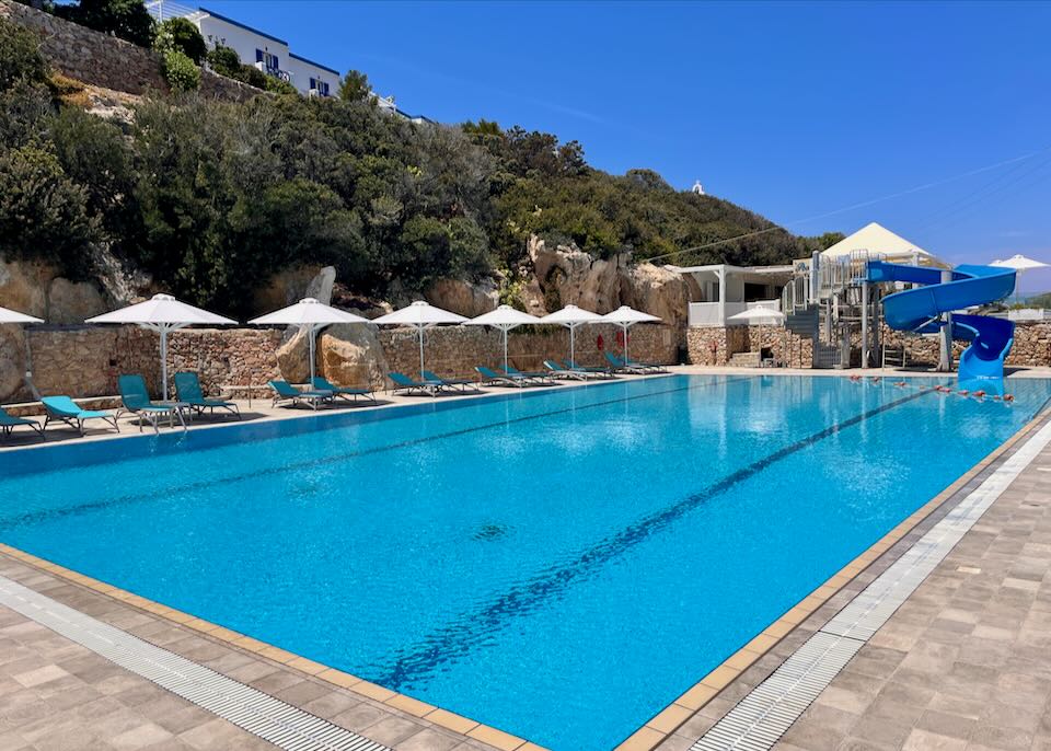 Large blue pool with water slide and sun loungers.