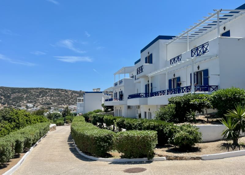 White and blue boxy Cycladic hotel next to a stony hillside